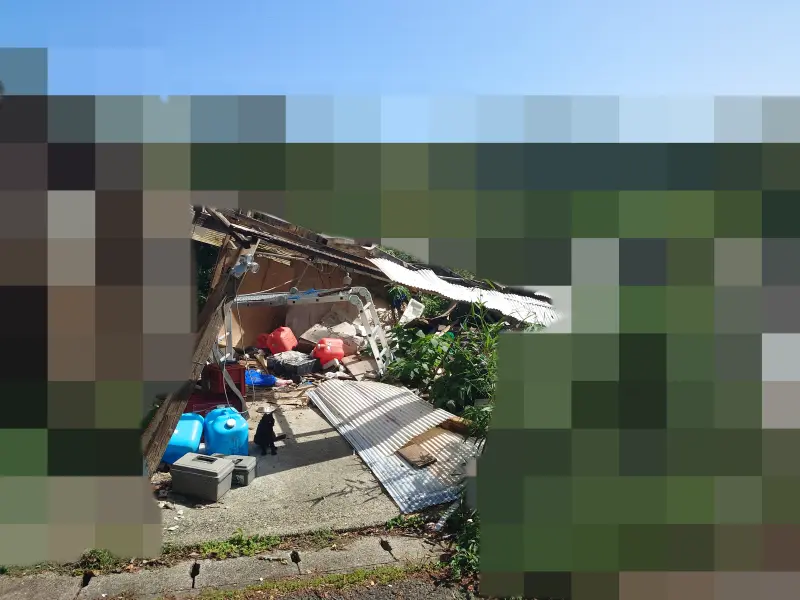 荒尾市での駐車場片付け前の様子。崩れた屋根やポリタンク、大量の資材が散乱しています